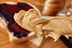 Swirls of creamy peanut butter on knife with bread and jelly in soft focus in background. Macro with extremely shallow dof.